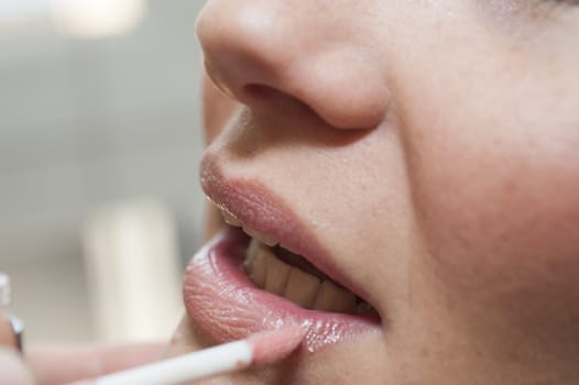 Closeup detail of a woman applying lip gloss makeup with a brush