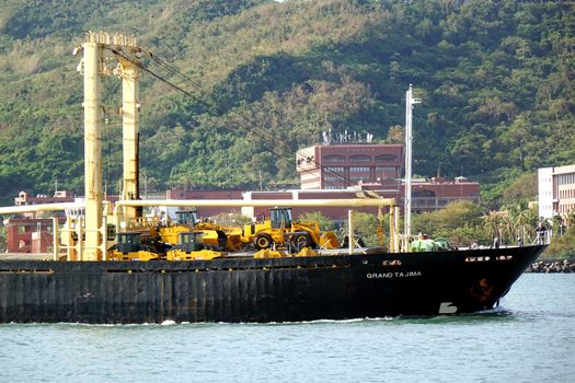 KAOHSIUNG, TAIWAN -- AUGUST 12, 2015: The Panamanian freighter Grand Tajima enters Kaohsiung Port with a cargo of construction equipment and excavators.
