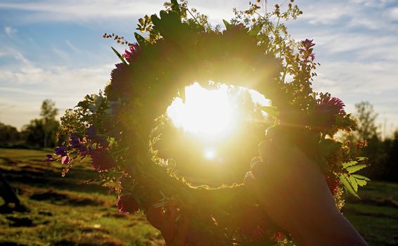 Hands with a wreath of Midsummer flowers against the sunset