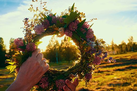 Hands with a wreath of Midsummer flowers against the sunset