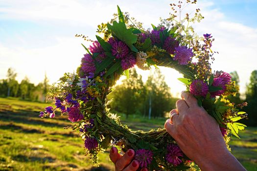 Hands with a wreath of Midsummer flowers against the sunset