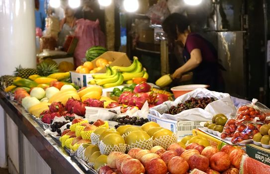 KAOHSIUNG, TAIWAN -- JUNE 26, 2014: A vendor selling a variety of fruit at a local market prepares a pineapple for a customer.
