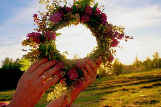 Hands with a wreath of Midsummer flowers against the sunset