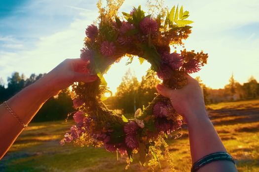 Hands with a wreath of Midsummer flowers against the sunset