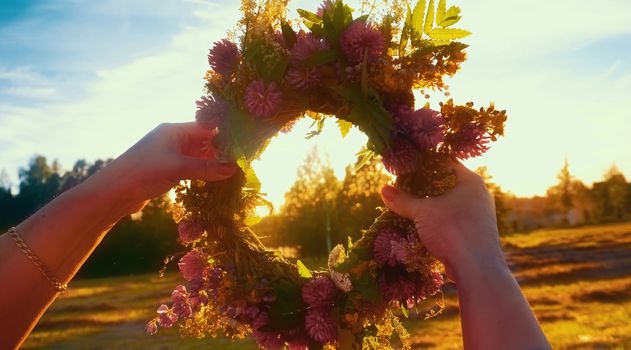 Hands with a wreath of Midsummer flowers against the sunset