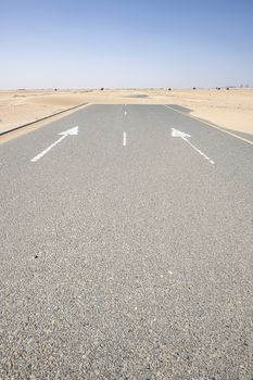 Vertical shot of an empty road covered by sand in the desert with blue sky. Large copy space on the tarmac