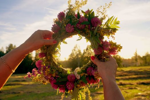 Hands with a wreath of Midsummer flowers against the sunset