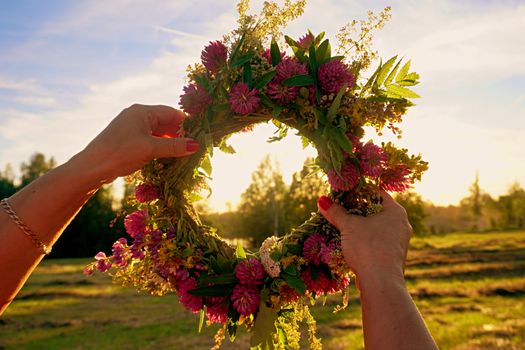 Hands with a wreath of Midsummer flowers against the sunset