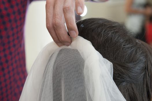 Closeup detail of female bridal womens hair styling being styled at hairdresser salon with head piece veil