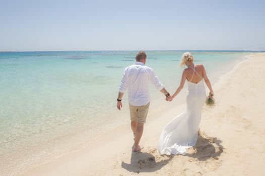 Beautiful couple walking together at a tropical beach paradise on wedding day in white gown dress with ocean view