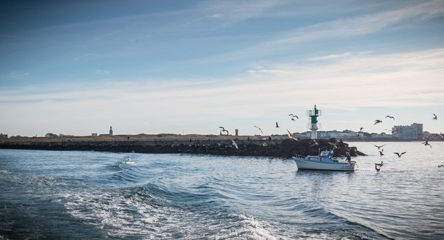 Saint Gilles Croix de Vie, France - September 16, 2018: Small fishing boat entering the harbor accompanied by seagulls on a summer day