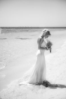 Beautiful woman bride at a tropical beach paradise on wedding day holding flower bouquet in gown dress with ocean view black and white