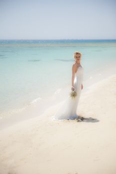 Beautiful woman bride at a tropical beach paradise on wedding day in white gown dress with ocean view