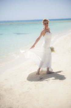 Beautiful woman bride at a tropical beach paradise on wedding day in white gown dress with ocean view