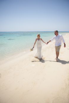 Beautiful couple walking together at a tropical beach paradise on wedding day in white gown dress with ocean view