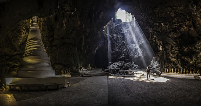 Male tourists stand looking ray of light at Khao Luang Cave