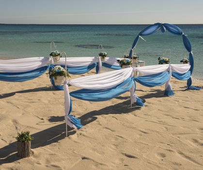 Setup of wedding day marriage aisle with drapes and arch on sandy tropical beach paradise to open ocean background 