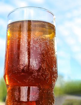 Refreshing orange summer cocktails with cola and ice against a blue sky background. 