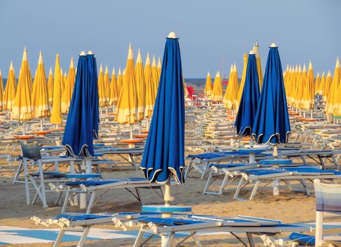 Blue and yellow umbrellas and sunbeds on the beach of Rimini in Italy