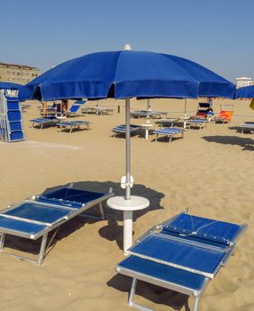 Blue open umbrella and sunbeds on the beach of Rimini in Italy