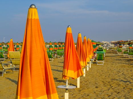 Orange closed umbrellas on the beach of Rimini in Italy