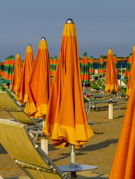 Orange closed umbrellas on the beach of Rimini in Italy