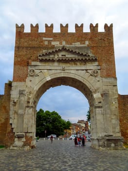Rimini, Italy - June 14, 2017: Unidentified people walk under Augustus Arch - the ancient romanesque gate and the historical landmark of Rimini, Italy.