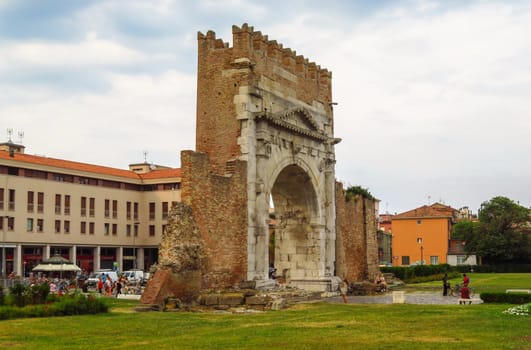 Rimini, Italy - June 14, 2017: Unidentified people walk under Augustus Arch - the ancient romanesque gate and the historical landmark of Rimini, Italy.