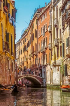 Venice, Italy - June 20, 2017: View from water canal to old buildings in Venice, Italy. Unrecognizable people are walking down the street in the old center.