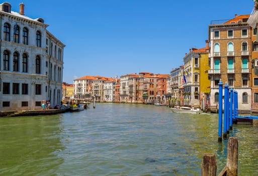 Venice, Italy - June 20, 2017: View from water canal to old buildings in Venice, Italy. Unrecognizable people are walking down the street in the old center.