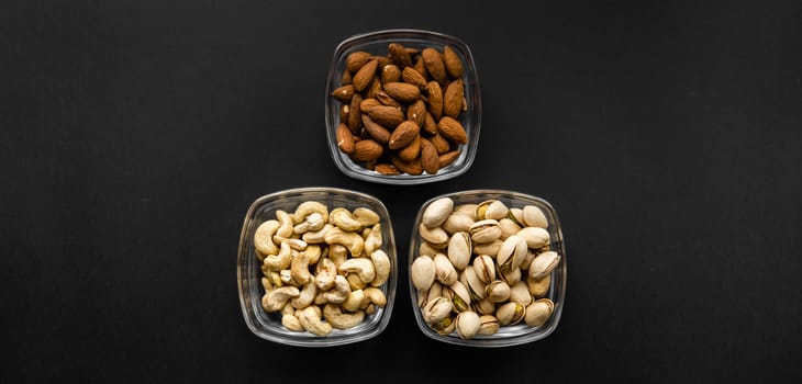 Almond, pistachio and cashew in a small plates which standing on a black table. Nuts is a healthy vegetarian protein and nutritious food