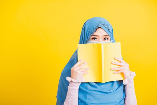 Asian Muslim Arab, Happy beautiful young woman religious wear veil hijab and face mask to prevent coronavirus she student hold books close face, isolated on yellow background, Back to college