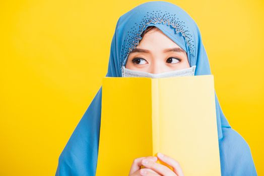 Asian Muslim Arab, Happy beautiful young woman religious wear veil hijab and face mask to prevent coronavirus she student hold books close face, isolated on yellow background, Back to college