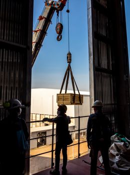 The crane carrying a wooden box of the radioactivity holder into the window on the factory floor