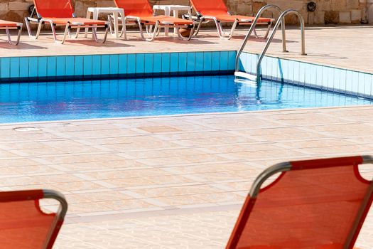 Swimming pool with empty sunbeds outside of vacation hotel. contemporary relax blue water pool  photography.  poolside with ladder and beach chairs in summertime. no people relax resort exterior.