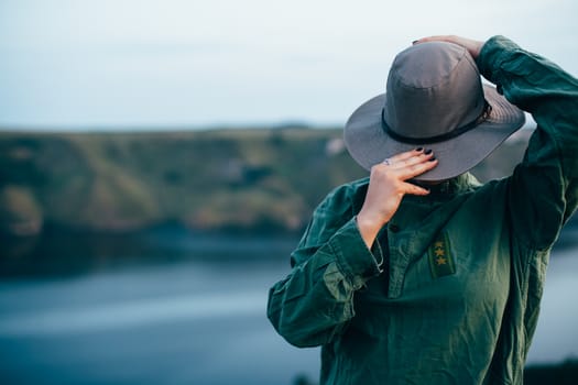 A girl stands on top of a mountain against the backdrop of a large canyon with a river. Portrait of a girl in a big hat covering her face.