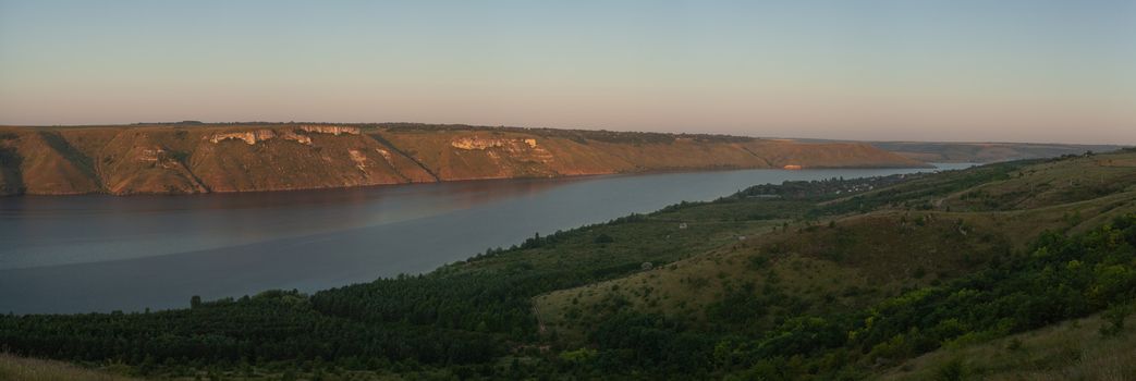 A large river on a background of rocky hills covered with trees.