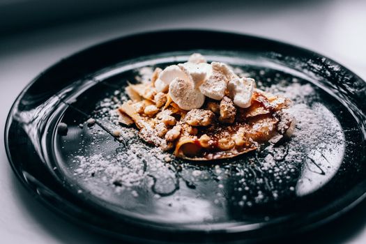 Plate with folded pancake caramel coated walnuts and marshmallows.