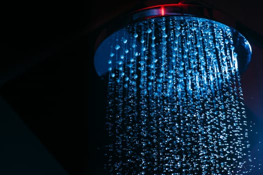 Drops of water fall from a watering can in the shower in blue light. Water drops close-up. Flow of water. Big round watering can macro photo.