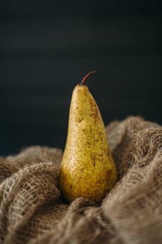 Still life with a pear standing on burlap on a dark wooden background.