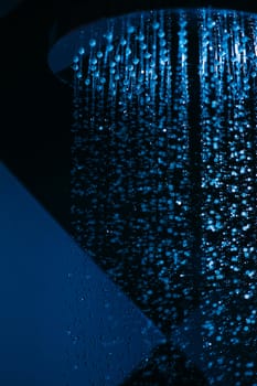 Drops of water fall from a watering can in the shower in blue light. Water drops close-up. Flow of water. A large round watering can in the shower.