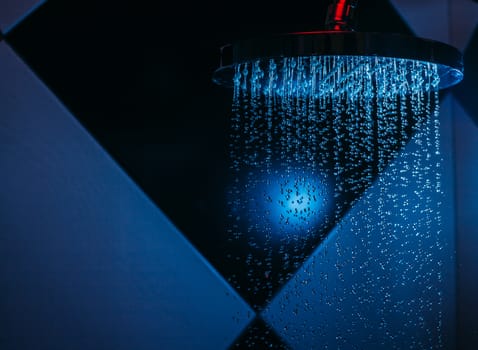 Drops of water fall from a watering can in the shower in blue light. Water drops close-up. Flow of water. Big round watering can.