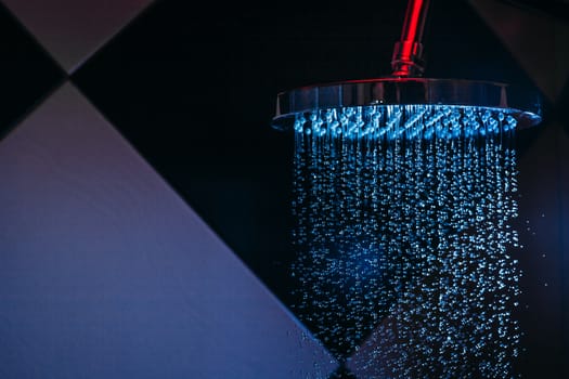 Drops of water fall from a watering can in the shower in blue light. Water drops close-up. Flow of water. Big round watering can.