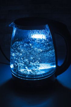 Boiling glass black teapot with blue backlight on a black background. Boiling water. Hot water is seething. Bubbles of air in the water.