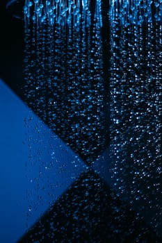 Drops of water fall from a watering can in the shower in blue light. Water drops close-up. Flow of water. Big round watering can macro photo.