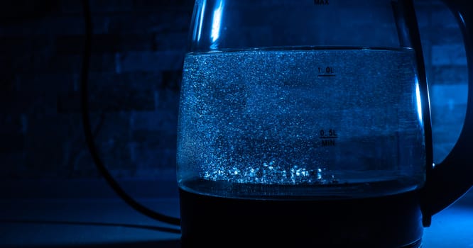 Boiling glass black teapot with blue backlight on a black background. Boiling water. Hot water is seething. Bubbles of air in the water.