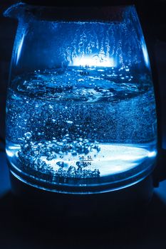 Boiling glass black teapot with blue backlight on a black background. Boiling water. Hot water is seething. Bubbles of air in the water.