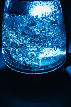 Boiling glass black teapot with blue backlight on a black background. Boiling water. Hot water is seething. Bubbles of air in the water.