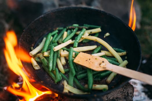 String beans in a pan. Cooking vegetables on an open fire. Food on a camping trip. Wooden spatula in a pan