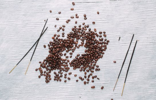 A scattering of coffee beans on a white wooden background with aromatic sticks.